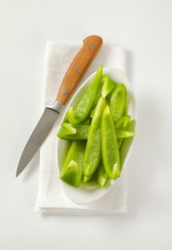 Sliced green bell pepper in white bowl and kitchen knife next to it