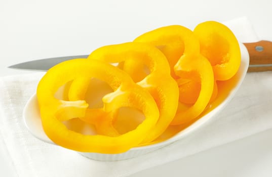 Sliced yellow bell pepper in white bowl and kitchen knife next to it