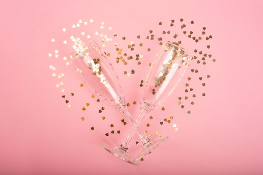 Valentines day champagne flutes glasses and heart shaped golden glitters on pink background with copy space for text