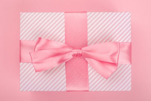 Valentines Day gift in a box wrapped in striped paper and tied with silk ribbon bow on pink background with copy space for text