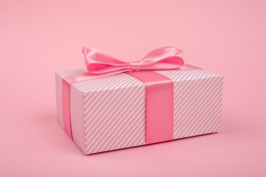 Valentines Day gift in a box wrapped in striped paper and tied with silk ribbon bow on pink background with copy space for text