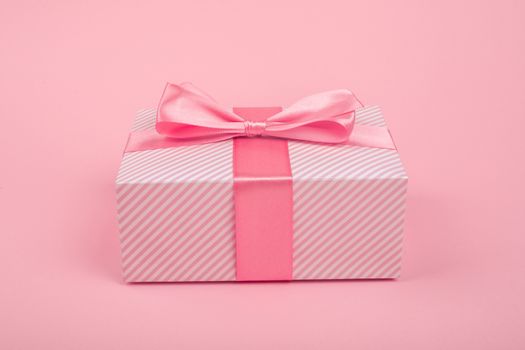 Valentines Day gift in a box wrapped in striped paper and tied with silk ribbon bow on pink background with copy space for text