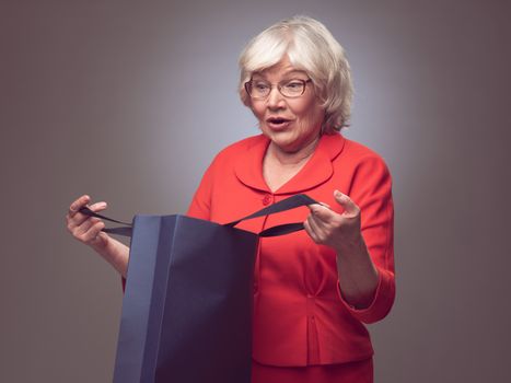 Surprised senior woman looking into paper bag , sale or gift concept