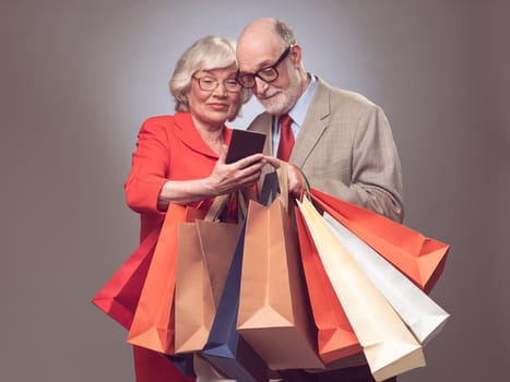 Happy elder couple with many shopping bags surfing the net online shopping concept