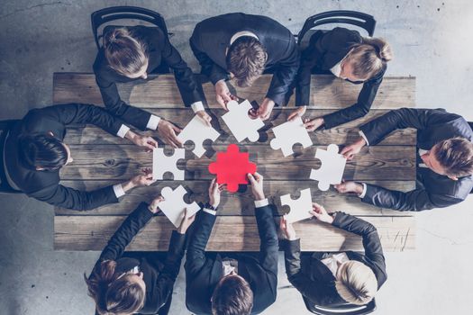 Businesspeople joining puzzle pieces on table, teamwork problem solution concept