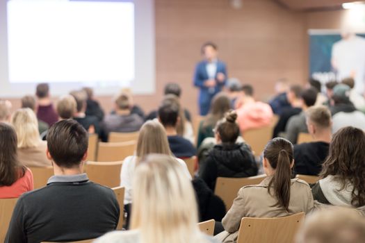 Speaker giving a talk in conference hall at business event. Audience at the conference hall. Business and Entrepreneurship concept. Focus on unrecognizable people in audience.