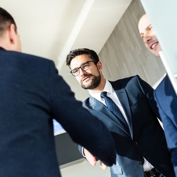 Group of confident business people greeting with a handshake at business meeting in modern office. Closing the deal agreement by shaking hands. Business and entrepreneurship success concept.