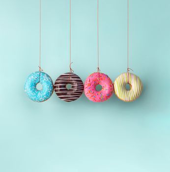 Four donuts hanging on the ropes. Harm of sugar, donuts time or healthy diet concept. Dependence on flavoring, diabetes problems, weight loss. Square shape. Copy space bottom