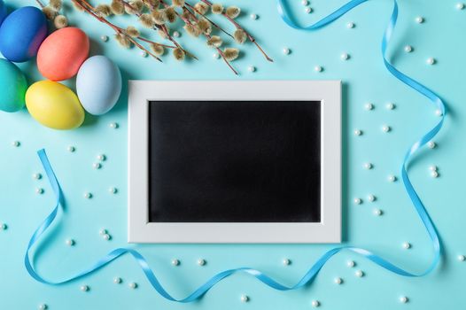 Orthodox Easter concept. Colorful eggs and pussy willow branches on blue background with empty chalkboard. Copy space for greetings, text or design. Top down view or flat lay