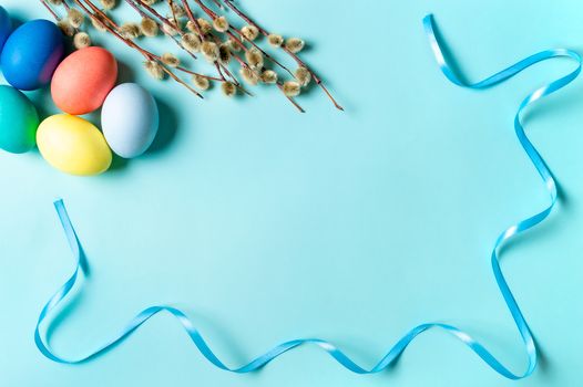 Orthodox Easter concept. Colorful eggs and pussy willow branches on blue background with empty chalkboard. Copy space for greetings, text or design. Top down view or flat lay