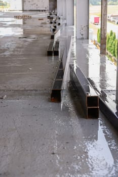 Big square metal pipes parts under rain on construction with sky in reflection.