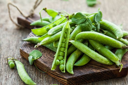 Green peas in pods with leaves on a wooden table