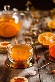 Orange and sea buckthorn tea in the glass cup and teapot on a wooden table