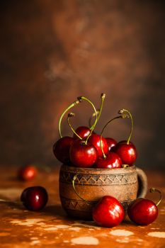 Fresh cherry berries in vintage ceramic cup on orange background. Copy space.