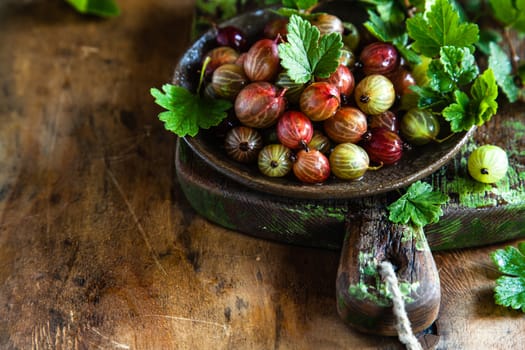 Gooseberries with leaves in a ceramic plate on a wooden background. Copy space.