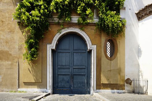 An old wooden blue arched door surrounded by hanging green branches