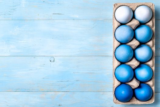 Easter concept. Ombre eggs in blue colors in cardboard packaging on blue wooden background with copy space for text. Top down view or flat lay. Classic blue colors in Easter 2020