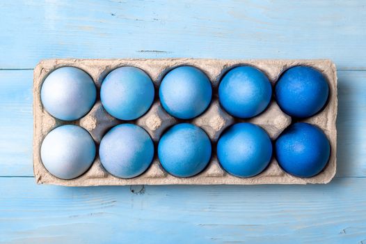 Easter concept. Ombre eggs in blue colors in cardboard packaging on blue wooden background. Top down view or flat lay. Classic blue colors in Easter 2020