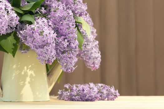 Vase in the form of an old vintage watering can with a bouquet of lilacs on table on a wooden background.