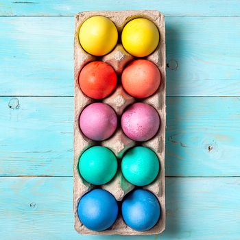 Easter concept. Colorful eggs in cardboard packaging on blue wooden background. Top down view or flat lay. Square