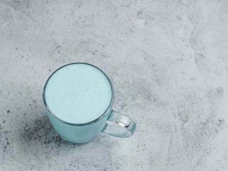 Trendy drink: Blue latte. Top view of hot butterfly pea latte or blue spirulina latte on gray cement textured background. Copy space for text. Top view or flat lay.