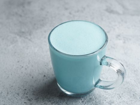 Trendy drink: Blue latte. Top view of hot butterfly pea latte or blue spirulina latte on gray cement textured background. Copy space for text.
