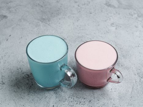 Trendy drink: Blue and pink latte. Hot butterfly pea latte or blue spirulina latte and pink beetroot or raspberry latte on gray cement textured background. Copy space.