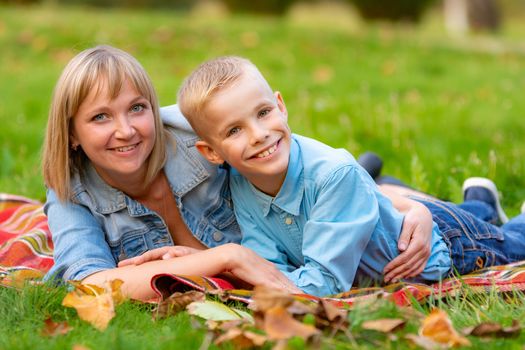 Young mom and teen son lie on bedspread on grass in city park