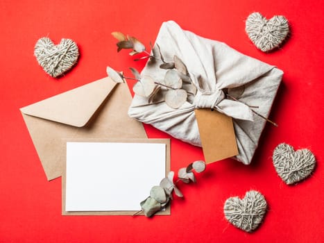 Zero waste Valentine's Day concept and mock up on red. Eco-friendly gift cloth wrapping in Furoshiki style, craft paper envelope,empty greetings card. Top down view or flat lay. Copy space for design