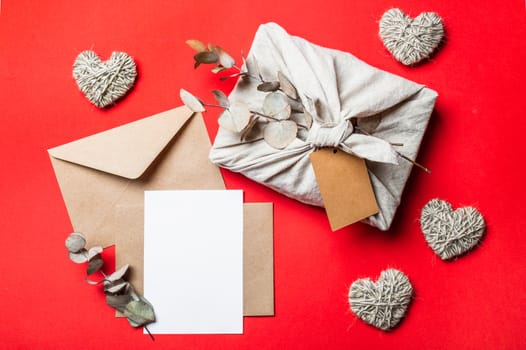 Zero waste Valentine's Day concept and mock up on red. Eco-friendly gift cloth wrapping in Furoshiki style, craft paper envelope,empty greetings card. Top down view or flat lay. Copy space for design