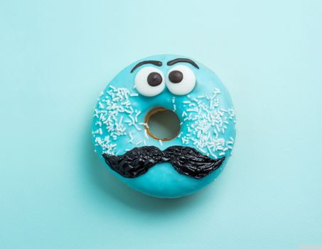 Blue glazed donut with mustache. Blue doughnut with funny face with mustache on blue background. Copy space for text. Masculinity or father day concept. Top view or flat lay