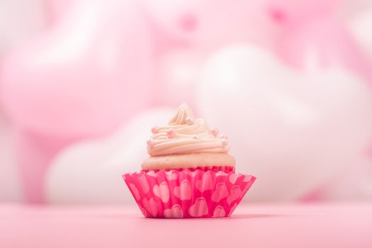 Valentine day love cupcake decorated with cream on pink and white party heart balloons background with copy space for text