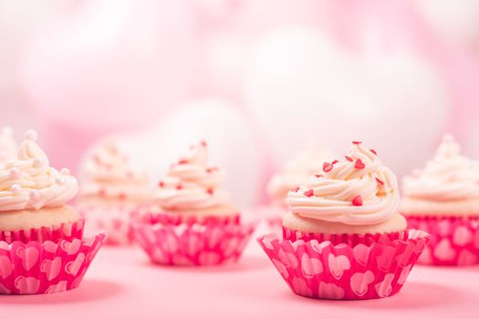 Valentine day love cupcakes decorated with cream and hearts on pink and white party balloons background with copy space for text