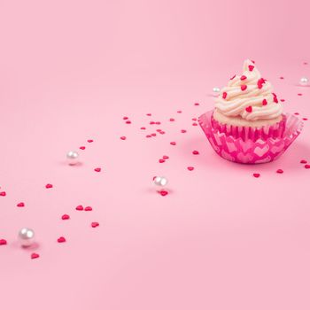 Valentine day love cupcake decorated with cream and hearts on pink background with copy space for text