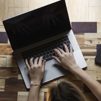 Woman's hands typing on laptop keyboard top view. Study and work online, freelance. Self employed or freelance woman, girl working with her laptop sitting at wooden table with a phone and ereader
