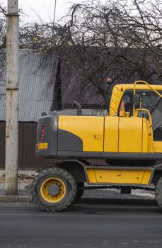 Yellow excavator standing on a road on construction site of the road on a street. Heavy industry. Construction of a road