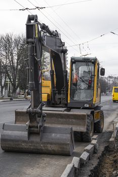 Yellow excavator standing on a road on construction site of the road on a street. Heavy industry. Construction of a road