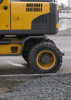 Yellow excavator standing on a road on construction site of the road on a street. Heavy industry. Construction of a road