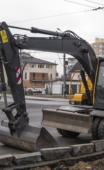 Yellow excavator standing on a road on construction site of the road on a street. Heavy industry. Construction of a road