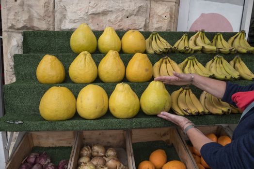 woman showing big etrog citrus fruit , apples onion and bananas on the market in eilat in israel