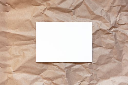 Crumpled craft brown paper background with white sheet in middle. Copy space. Horizontal. DIY, handicraft, back to school, ecology, plastic free concept, harvesting for mock up. Flat lay, top view.