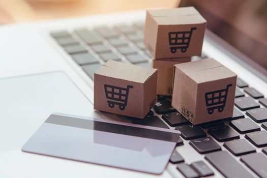 Online shopping - Paper cartons or parcel with a shopping cart logo and credit card on a laptop keyboard. Shopping service on The online web and offers home delivery.

