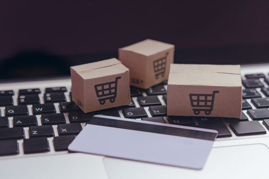 Online shopping - Paper cartons or parcel with a shopping cart logo and credit card on a laptop keyboard. Shopping service on The online web and offers home delivery.

