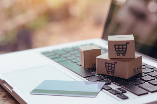 Online shopping - Paper cartons or parcel with a shopping cart logo and credit card on a laptop keyboard. Shopping service on The online web and offers home delivery.

