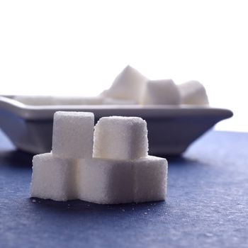 Sugar Cubes with Sugar in white plate on blue background