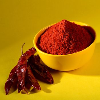 chili powder in yellow bowl on yellow background. Red chilly pepper