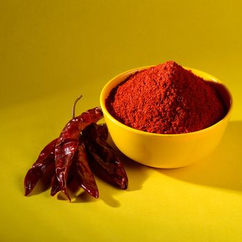 chili powder in yellow bowl on yellow background. Red chilly pepper