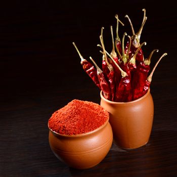 chilly powder with red chilly in clay pots, dried chillies on dark background