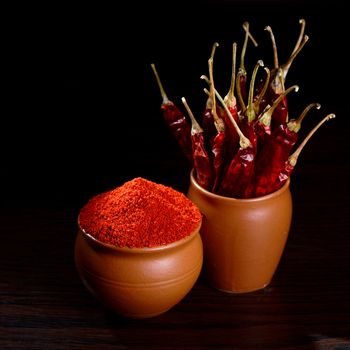 chilly powder with red chilly in clay pots, dried chillies on dark background