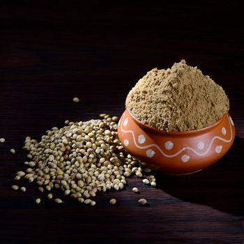 Coriander seeds and Powdered coriander in clay pot on wooden background.